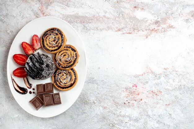 Vista superior deliciosas galletas con pastel de chocolate y fresas en el escritorio blanco