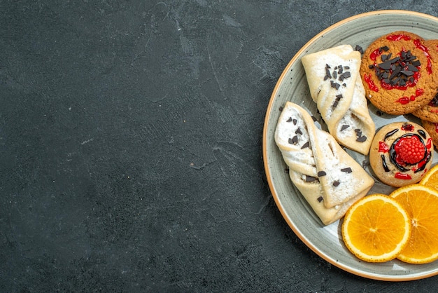 Vista superior deliciosas galletas con pasteles afrutados y rodajas de naranja sobre fondo oscuro pastel dulce de frutas pastel té azúcar