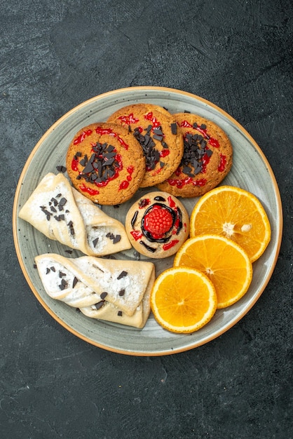 Vista superior deliciosas galletas con pasteles afrutados y rodajas de naranja sobre el fondo oscuro pastel dulce de frutas pastel té azúcar