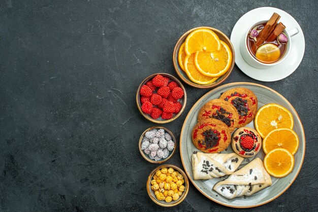 Vista superior deliciosas galletas con pasteles, rodajas de naranja, nueces y taza de té en el fondo oscuro, té, nuez, galleta, galleta, pastel dulce