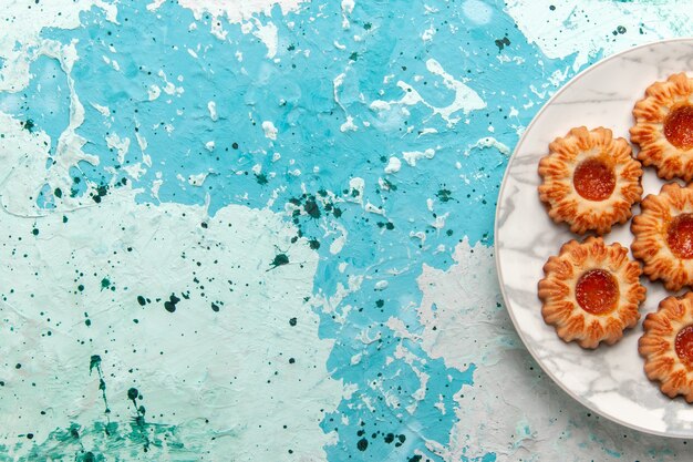 Vista superior de deliciosas galletas redondas formadas con mermelada dentro de la placa en el escritorio azul claro, azúcar, galleta, masa, pastel, hornear