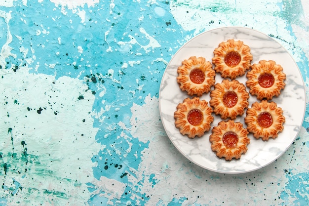 Vista superior de deliciosas galletas redondas formadas con mermelada dentro de la placa sobre el fondo azul claro, azúcar, galleta, masa de galletas dulces, hornear