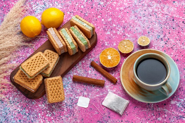 Vista superior de deliciosas galletas sándwich con té de limón y canela en el escritorio rosa.