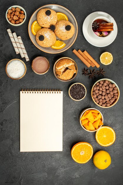 Vista superior deliciosas galletas con una taza de té y rodajas de naranja en el piso oscuro pastel pastel postre azúcar té galleta