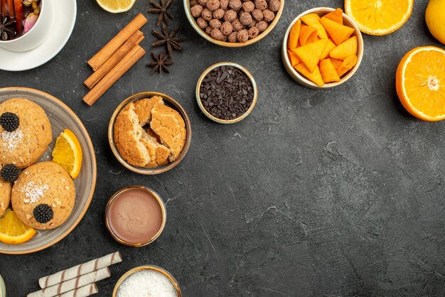 Vista superior deliciosas galletas con una taza de té y rodajas de naranja sobre una superficie oscura pastel de azúcar postre galleta té