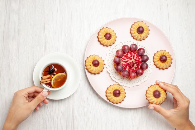 Vista superior deliciosas galletas de uva con una taza de té en la mesa blanca, pastel de galletas de postre dulce