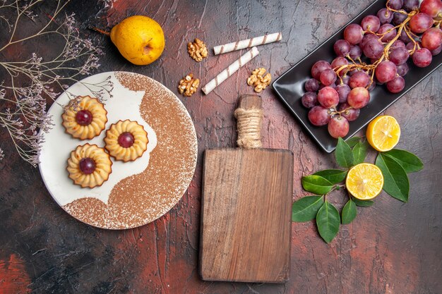 Vista superior deliciosas galletas con uvas en el piso oscuro pastel dulce galleta azúcar