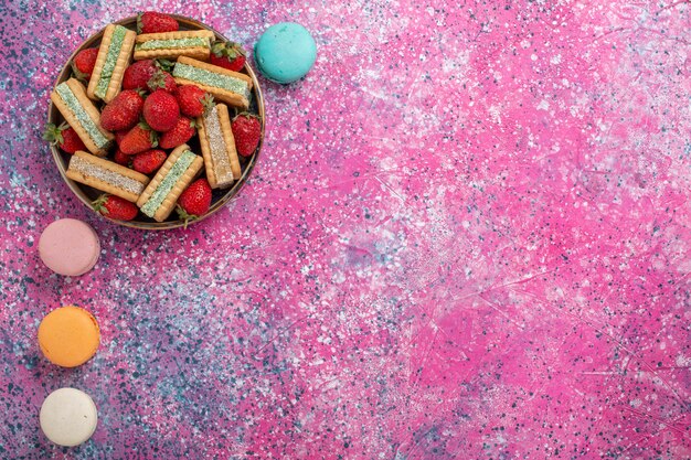 Foto gratuita vista superior de deliciosas galletas waffle con fresas rojas frescas y macarons franceses en superficie rosa