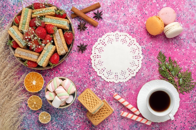 Vista superior de deliciosas galletas waffle con fresas rojas frescas y taza de té en superficie rosa