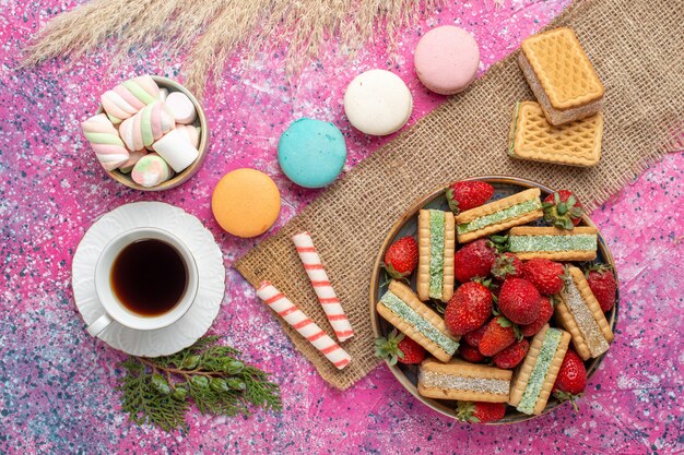 Vista superior de deliciosas galletas waffle con macarons franceses y té en superficie rosa