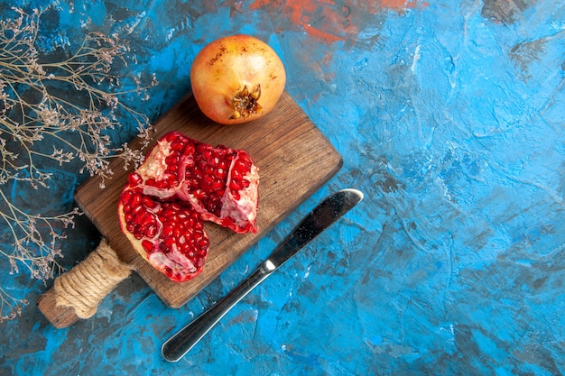 Vista superior deliciosas granadas en el cuchillo de cena de tabla de cortar sobre fondo azul.