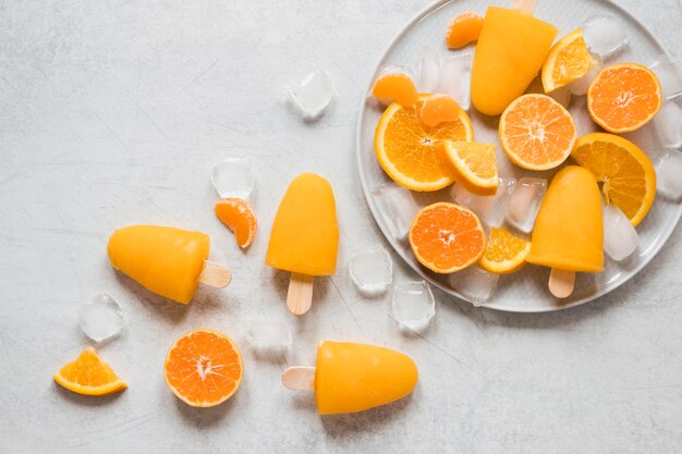 Vista superior de deliciosas paletas en plato con hielo y naranja