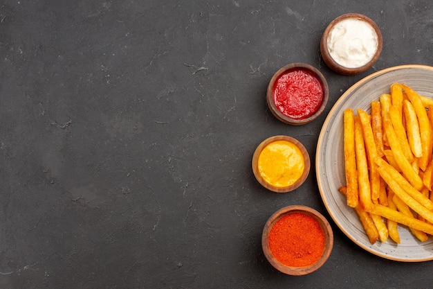 Vista superior deliciosas papas fritas con condimentos en el fondo oscuro comida rápida hamburguesa de plato de papa