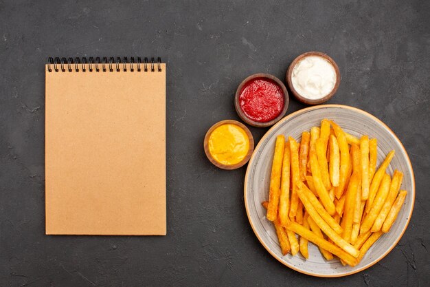 Vista superior deliciosas papas fritas con condimentos en el fondo oscuro comida rápida hamburguesa de plato de papa