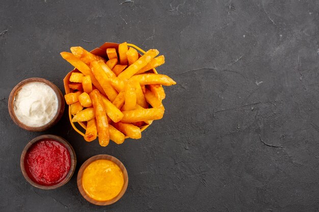 Vista superior deliciosas papas fritas con condimentos en el fondo oscuro, comida rápida, plato de papa, hamburguesa, comida