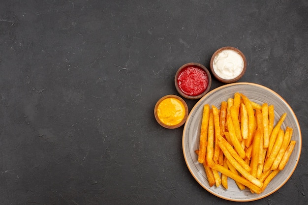 Vista superior deliciosas papas fritas con condimentos sobre fondo oscuro, comida, papa, comida rápida, hamburguesa, plato