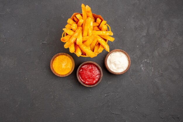 Vista superior deliciosas papas fritas con condimentos sobre fondo oscuro hamburguesa comida rápida plato de papa