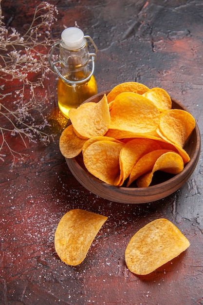 Vista superior de deliciosas papas fritas crujientes caseras dentro y fuera de la olla marrón y botella de aceite sobre fondo oscuro