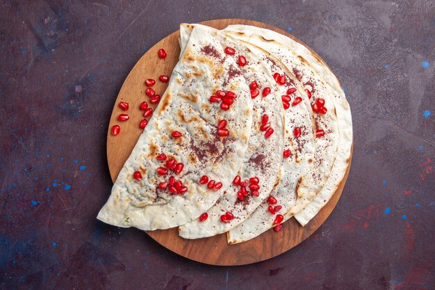 Vista superior de deliciosas pitas de carne qutabs con granadas rojas frescas en la superficie de color púrpura oscuro harina de masa de carne pita