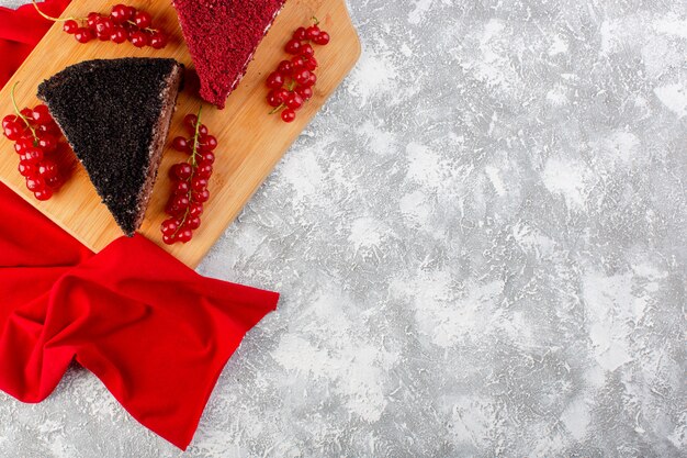 Vista superior de deliciosas rebanadas de pastel con crema de chocolate y frutas en el escritorio de madera con dulce de galleta de pastel de tejido rojo