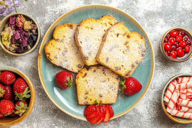 Vista superior de deliciosas rebanadas de pastel con fresas y dulces a la luz