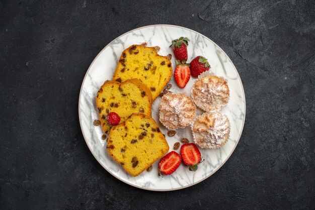 Vista superior de deliciosas rebanadas de pastel con fresas rojas frescas sobre una superficie gris oscuro