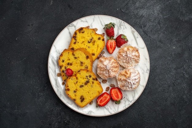 Vista superior de deliciosas rebanadas de pastel con fresas rojas frescas sobre una superficie gris oscuro