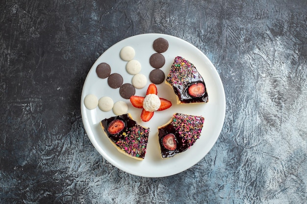 Vista superior de deliciosas rebanadas de pastel con pequeñas galletas en superficie oscura