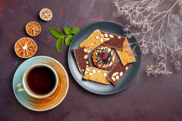 Vista superior de deliciosas rebanadas de pastel con poco de galleta y una taza de té en el fondo oscuro galleta galleta postre pastel té dulce
