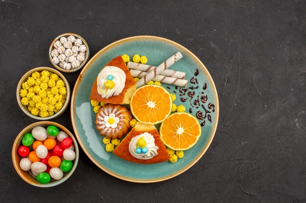 Vista superior de deliciosas rebanadas de pastel con rodajas de mandarinas y dulces en la oscuridad