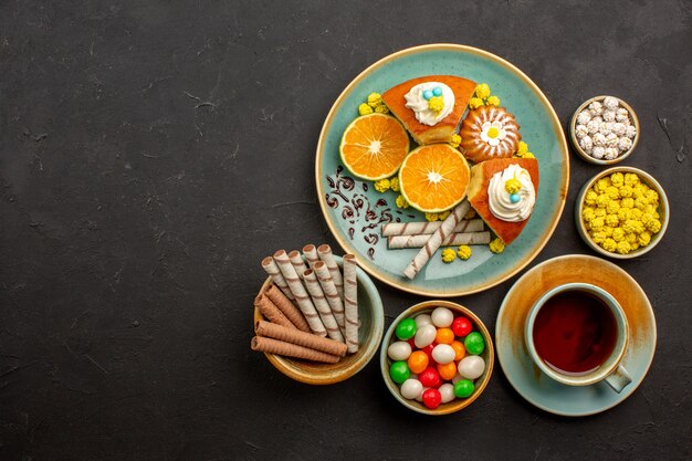 Vista superior de deliciosas rebanadas de pastel con té de mandarinas frescas y dulces en la oscuridad