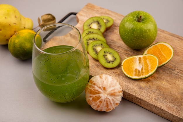 Foto gratuita vista superior de deliciosas rodajas de kiwi picado con mandarina y manzana en una tabla de cocina de madera con jugo de kiwi fresco