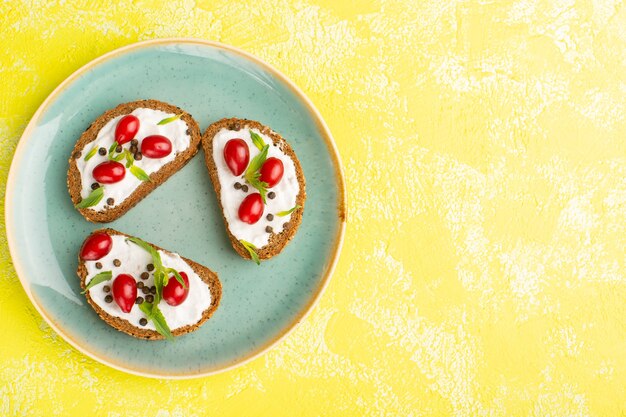 Vista superior de deliciosas tostadas de pan con crema agria y cornejos dentro de la placa azul sobre la superficie amarilla.