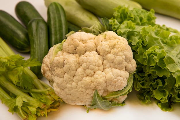 Vista superior de deliciosas verduras como coliflor, lechuga, apio, pepinos y calabacines aislados sobre un fondo blanco.