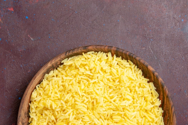 Foto gratuita vista superior del delicioso arroz cocido dentro de la placa marrón en el escritorio oscuro