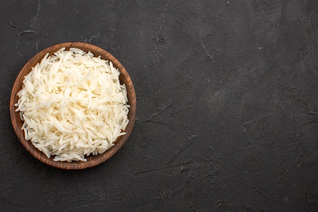 Vista superior delicioso arroz cocido llano sabroso arroz dentro de la placa marrón en el espacio oscuro