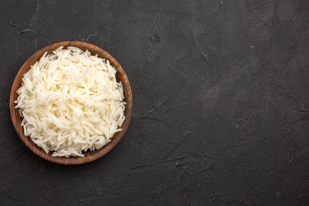 Vista superior delicioso arroz cocido llano sabroso arroz dentro de la placa marrón en el espacio oscuro