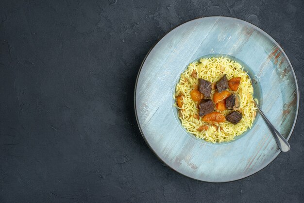 Vista superior del delicioso arroz cocido pilaf con albaricoques secos y rodajas de carne dentro de la placa sobre una superficie oscura