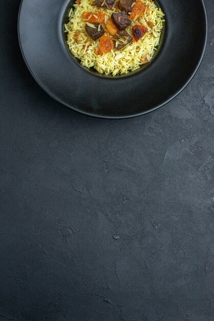 Vista superior del delicioso arroz cocido pilaf con albaricoques secos y rodajas de carne dentro de la placa sobre una superficie oscura