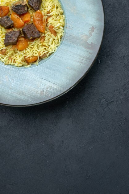 Vista superior del delicioso arroz cocido pilaf con albaricoques secos y rodajas de carne dentro de la placa sobre una superficie oscura