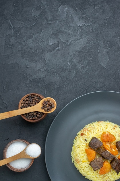 Vista superior del delicioso arroz cocido pilaf con rodajas de carne y condimentos en una superficie oscura