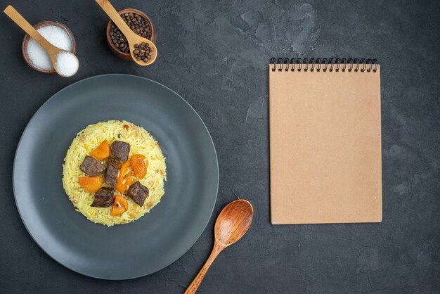 Vista superior del delicioso arroz cocido pilaf con rodajas de carne y condimentos en una superficie oscura