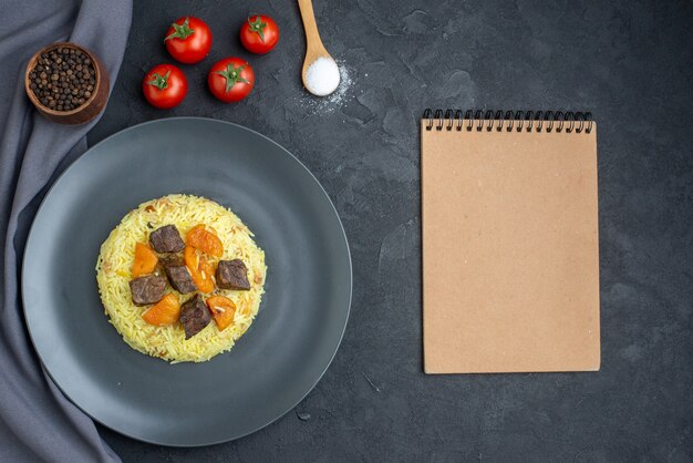 Vista superior delicioso arroz cocido pilaf con rodajas de carne y tomates en superficie oscura