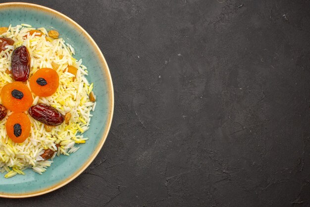 Vista superior del delicioso arroz plov cocido con diferentes pasas dentro de la placa sobre una superficie gris oscuro