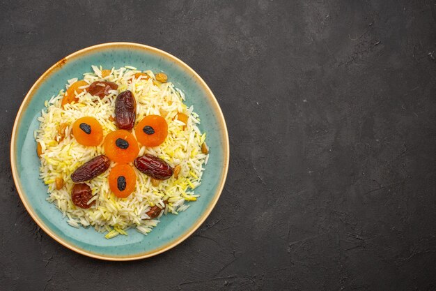 Vista superior del delicioso arroz plov cocido con diferentes pasas dentro de la placa sobre una superficie gris oscuro