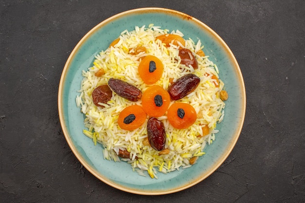 Vista superior del delicioso arroz plov cocido con diferentes pasas dentro de la placa sobre la superficie gris