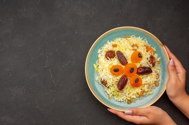 Vista superior del delicioso arroz plov cocido con diferentes pasas dentro de la placa sobre la superficie gris