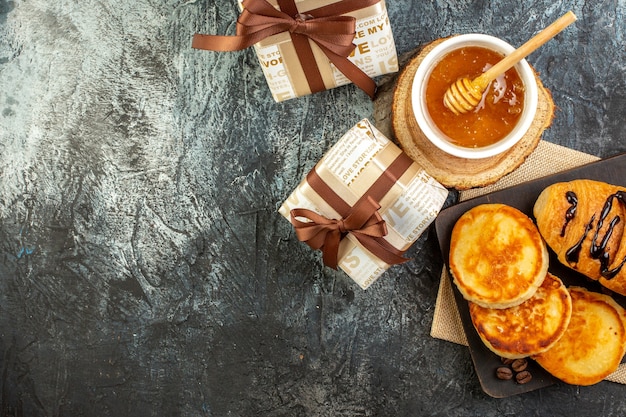 Vista superior del delicioso desayuno con panqueques en la tabla de cortar de madera miel hermosas cajas de regalo en superficie oscura