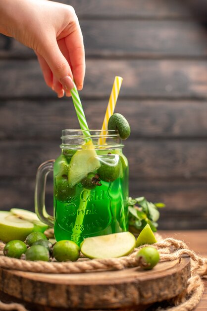 Vista superior del delicioso jugo de fruta fresca servido con manzana y feijoas mano sujetando el tubo sobre una tabla de cortar de madera