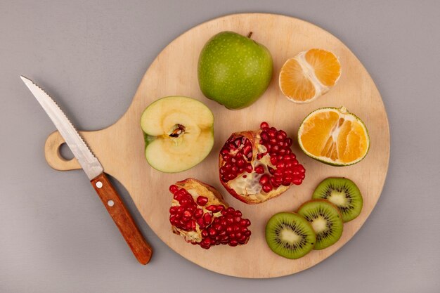 Vista superior del delicioso kiwi en rodajas con manzana, mandarina y granada en una tabla de cocina de madera con cuchillo